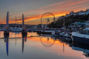 Torquay bei Sonnenuntergang. Die Küstenstadt erstrahlt in warmen, goldenen Farben, während die untergehende Sonne den Himmel und das glitzernde Meer in sanfte Orangetöne taucht.