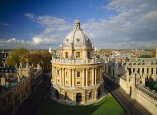 Die John Radcliffe Camera in Oxford, ein ikonisches rundes Gebäude aus honigfarbenem Stein. Umgeben von gepflegten Rasenflächen und historischen Gebäuden.