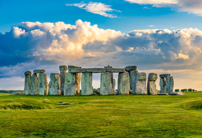 Stonehenge, der beeindruckende Steinkreis, vor einem satten grünen Vordergrund. Die mächtigen, uralten Steine ragen majestätisch gegen den Himmel, der von imposanten Wolken bedeckt ist.