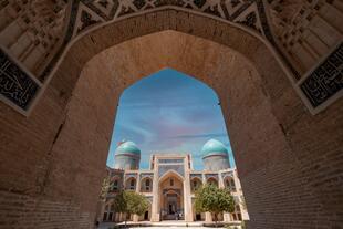 Zu sehen ist die Miri-Arab-Medrese in Buchara, durch ein Tor eingerahmt, das den Blick auf die majestätische Fassade freigibt. 