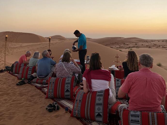 Reisegruppe auf einer Oman Reise sitzt bei Sonnenuntergang in der Wüste