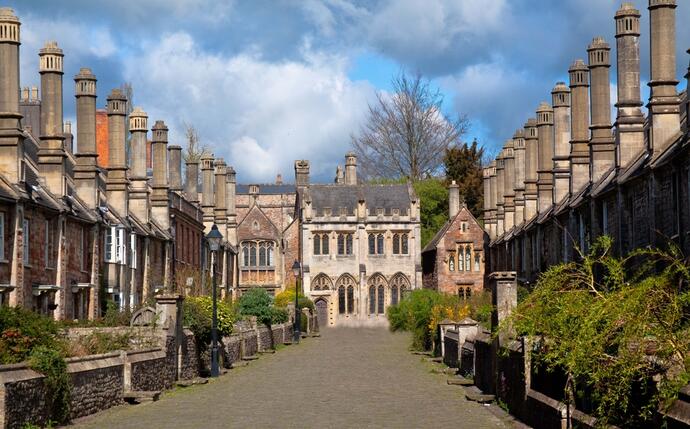 Wells Vicar's Close, eine historische Straße in Wells, Somerset. Die gut erhaltenen, georgianischen Häuser mit ihren charmanten Fassaden und bunten Blumenfenstern verlaufen entlang eines malerischen, gepflasterten Weges.